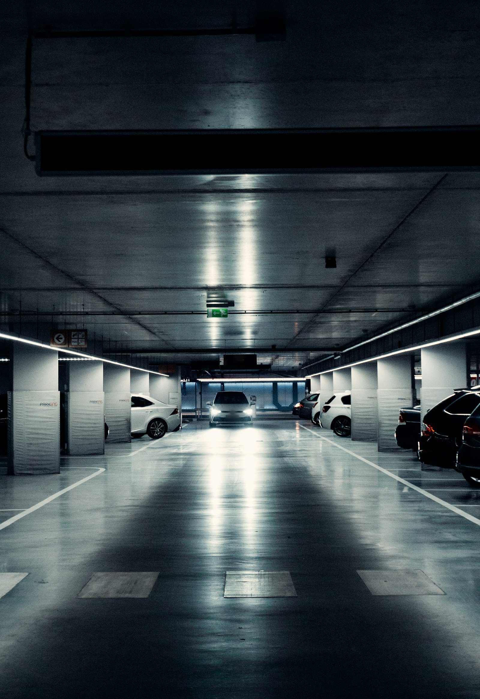 A lone car with headlights on in a dim parking garage at night